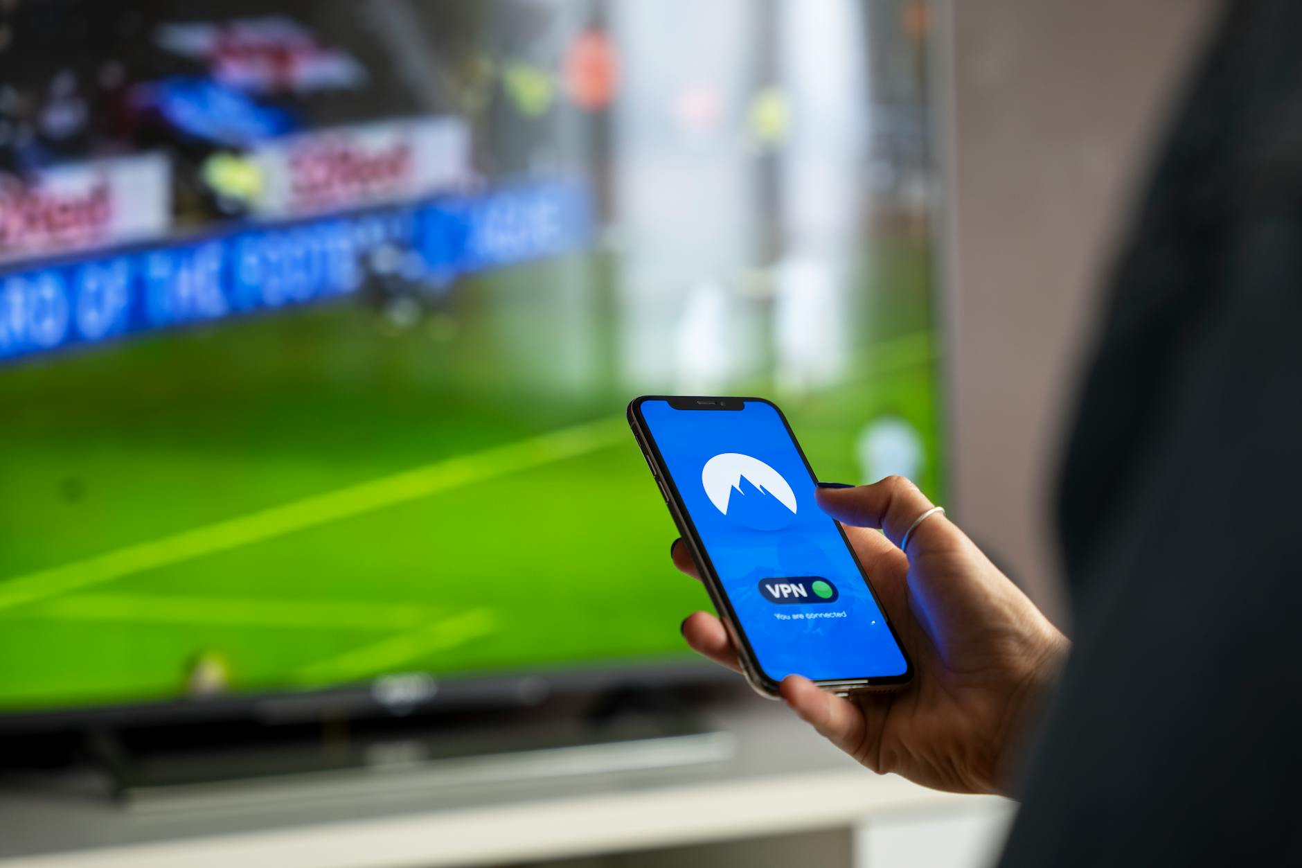 Osoba trzyma smartfon z aplikacją VPN, ogląda sport w telewizji