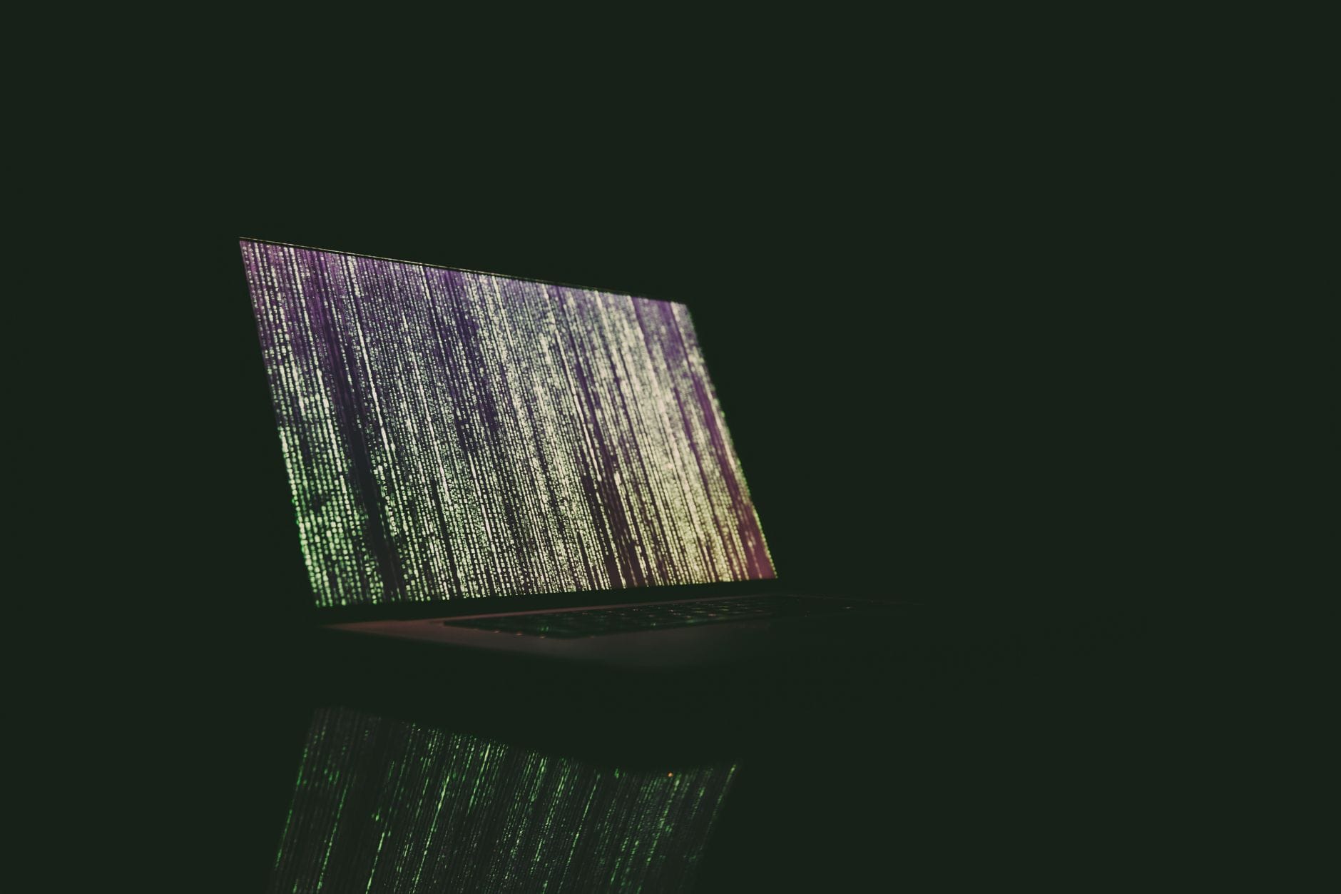 Szyfrowanie dysku w Windows i macOS krok po kroku dla zwykłego użytkownika Laptop z zielono-fioletowym kodem na ekranie w ciemnym pomieszczeniu